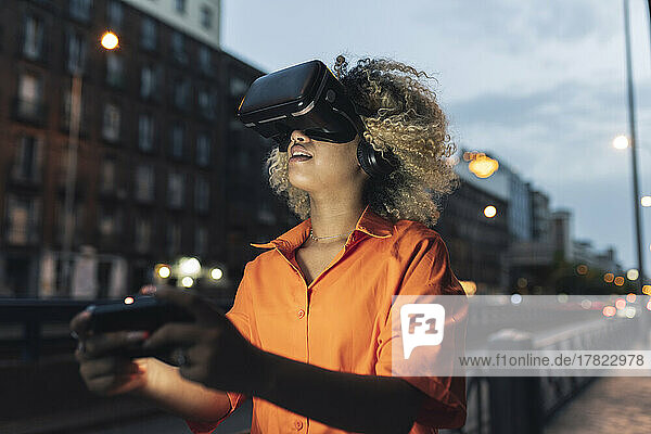 Woman holding controller wearing virtual reality headset at night