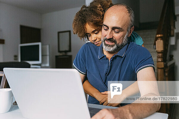 Mädchen umarmt Vater mit Laptop und arbeitet von zu Hause aus