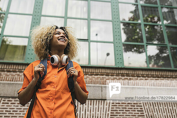 Smiling woman with headphones standing in front of building