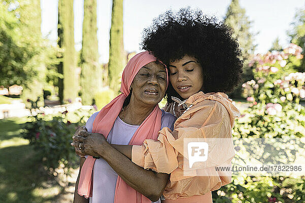 Mother and daughter with eyes closed embracing in park