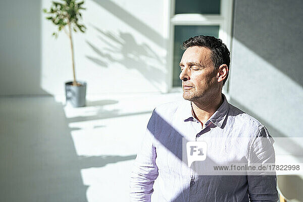 Businessman with eyes closed standing in sunlight at office