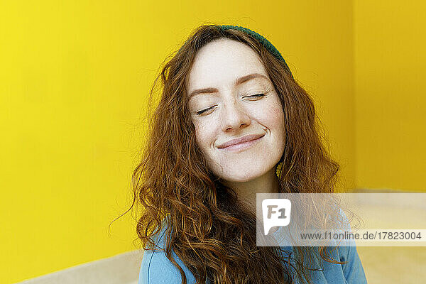 Smiling woman with eyes closed in front of yellow wall