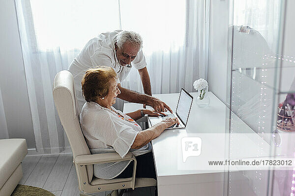 Smiling man explaining laptop to senior mother at home
