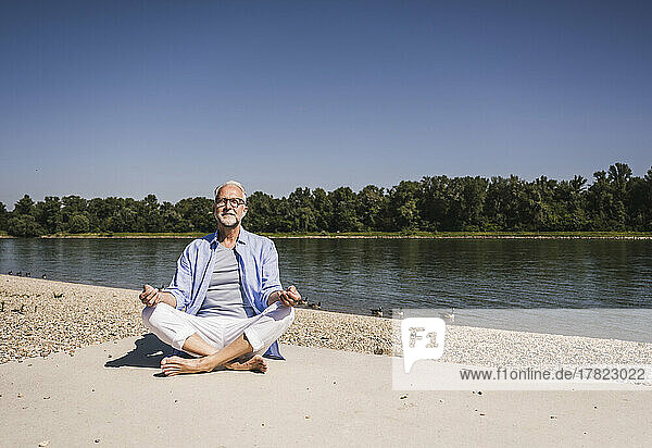 Smiling man meditating at riverbank