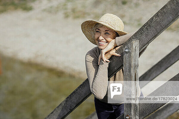 Lächelnde Frau mit Hut lehnt am Geländer