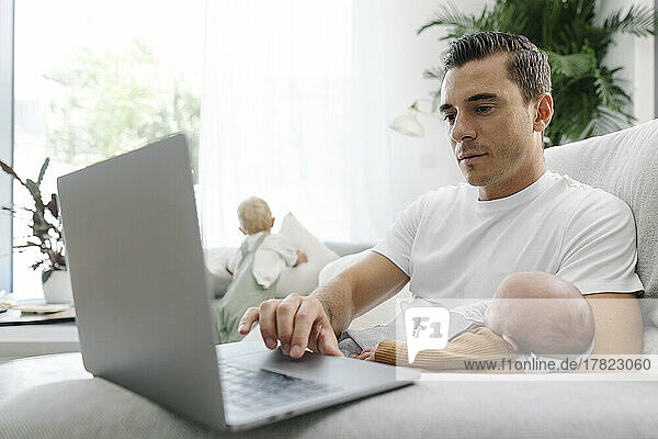 Man carrying baby in arm using laptop working from home