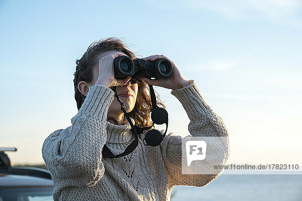 Young woman looking through binoculars on sunny day