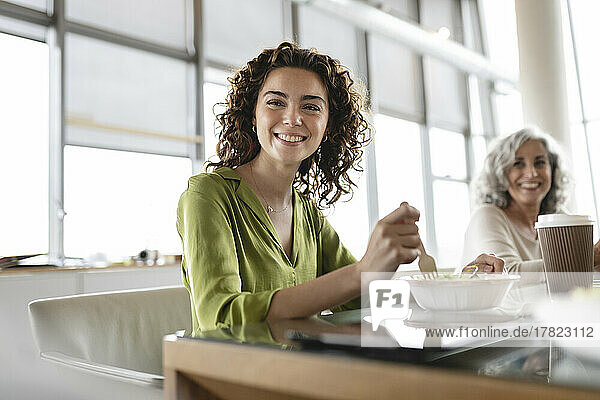 Glückliche junge Geschäftsfrau mit einer Schüssel Salat am Schreibtisch