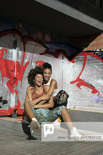 Happy friends embracing in front of graffiti wall on sunny day
