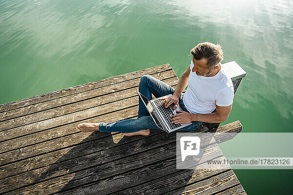 Freiberufler arbeitet am Laptop und sitzt am Pier über dem See