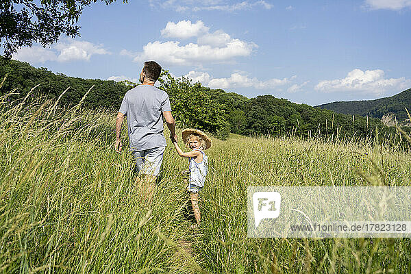 Father and daughter walking through field on sunny day