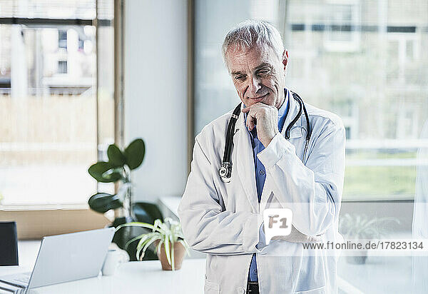 Thoughtful doctor with hand on chin standing in office