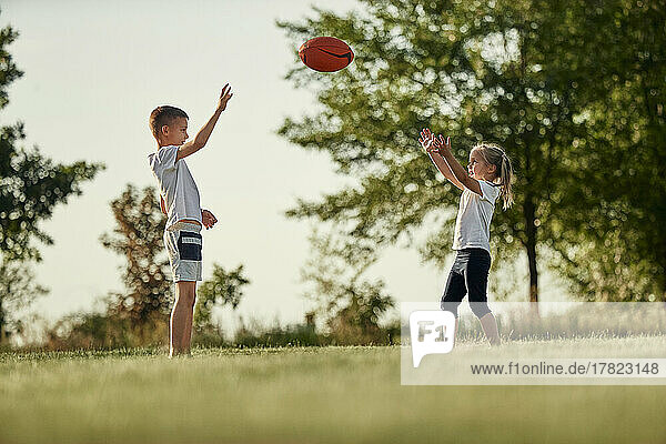 Brother and sister throwing rugby ball standing at sports field