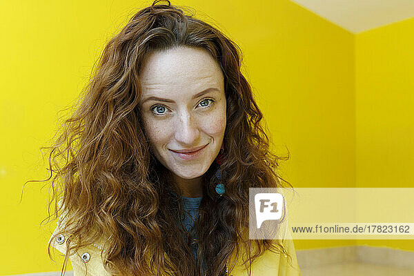 Smiling redhead woman in front of yellow wall at home