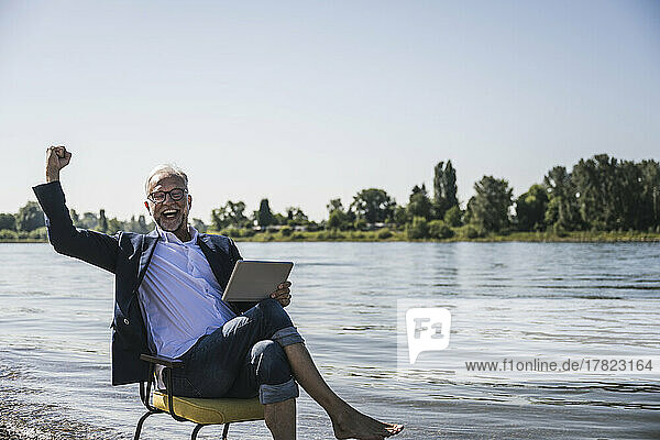 Happy man holding tablet PC gesturing at riverbank
