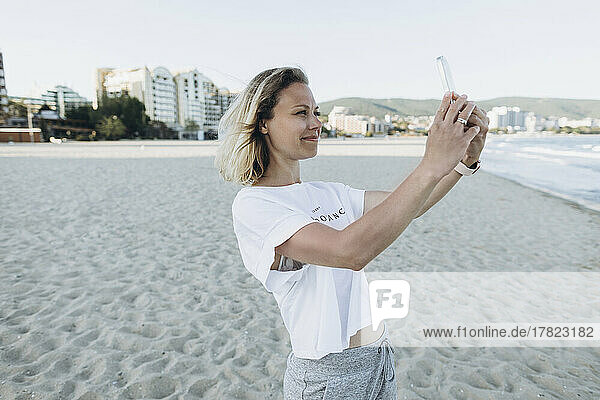 Smiling woman taking selfie through smart phone on beach