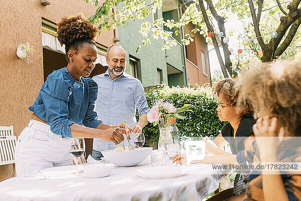 Smiling woman serving food to children standing by man at dining table in backyard