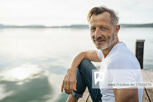 Smiling man sitting on jetty at lake