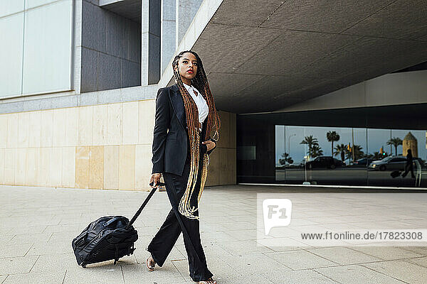 Young businesswoman with luggage walking outside office building