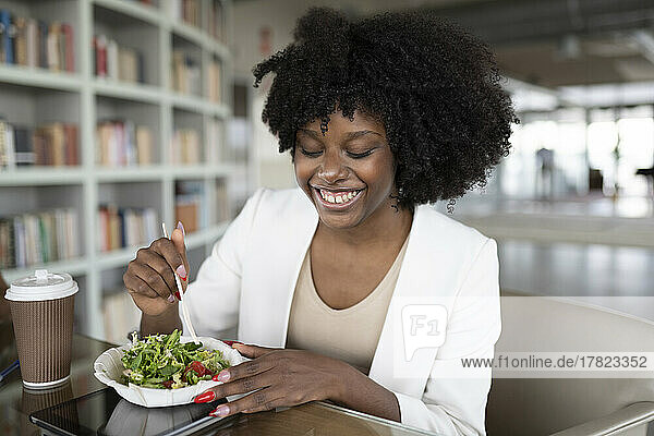 Happy businesswoman eating salad at desk in office