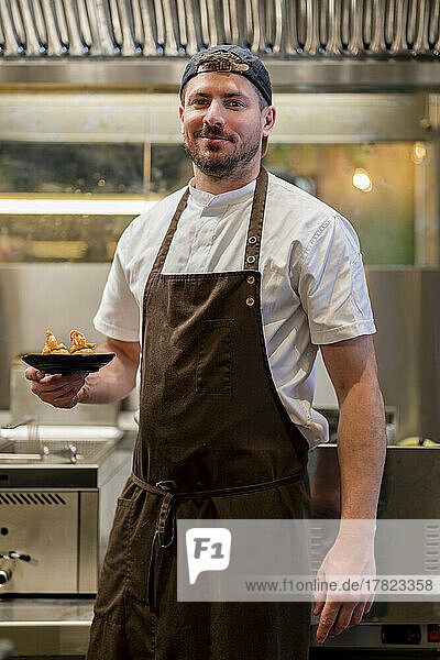 Chef with food in plate standing at restaurant kitchen