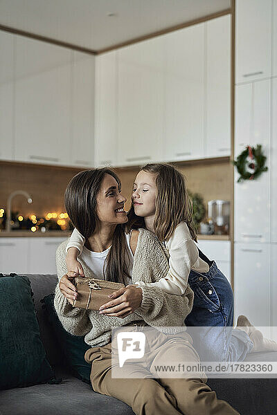 Girl giving gift to mother sitting on sofa in living room