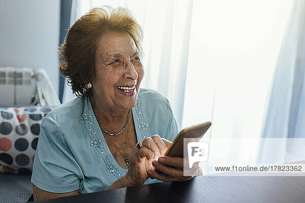 Happy senior woman with smart phone sitting at home