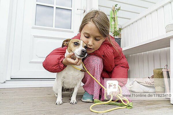 Girl with pet leash stroking dog at porch