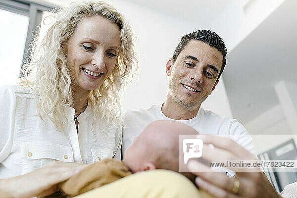 Smiling mother carrying baby on lap sitting by man at home