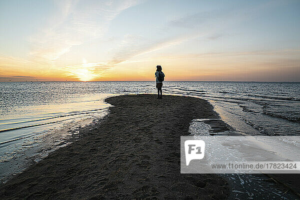Frau steht bei Sonnenuntergang an der Küste