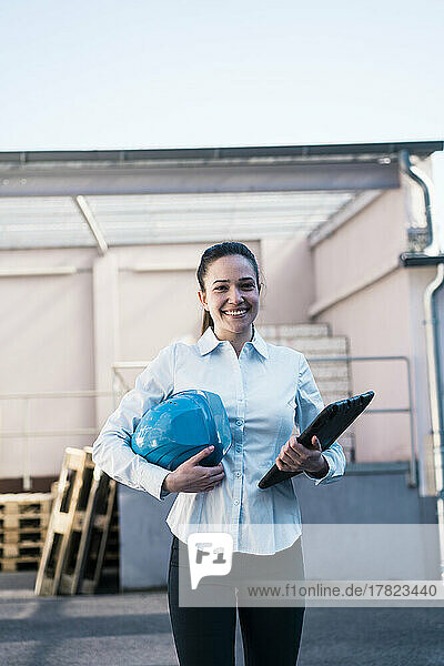 Happy female engineer with work helmet and tablet PC in industry