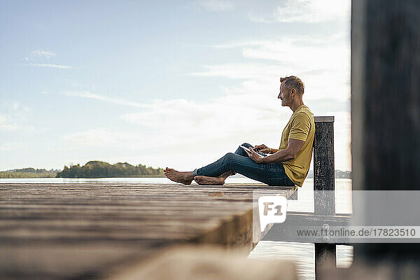 Mature man using tablet PC sitting on pier