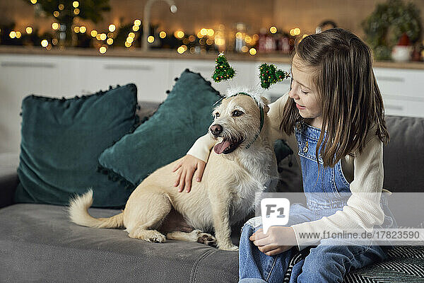Smiling girl with dog sitting on sofa at home