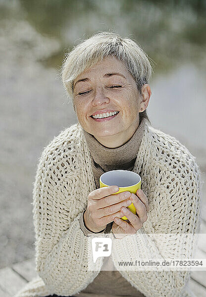Lächelnde reife Frau mit geschlossenen Augen  die eine Tasse hält