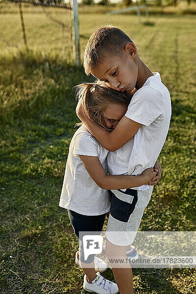 Brother hugging sister standing at sports field