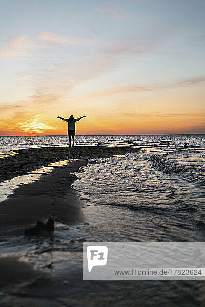 Young woman with arms outstretched standing on sea coast at sunset
