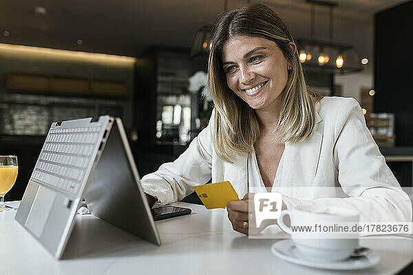 Glückliche Geschäftsfrau mit Kreditkarte beim Online-Einkauf per Laptop im Restaurant