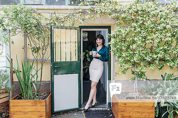 Smiling businesswoman with coffee cup at doorway