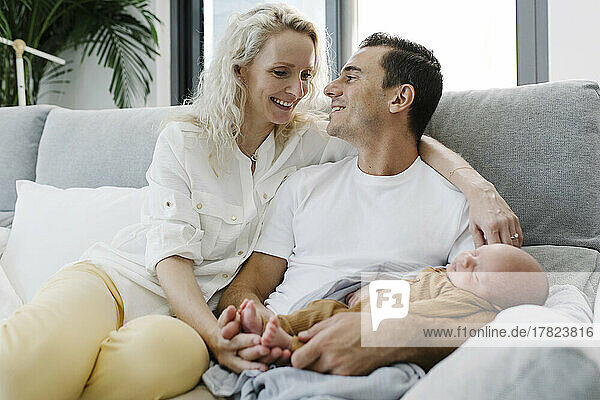 Mann mit Baby im Arm sitzt neben Frau auf Sofa zu Hause