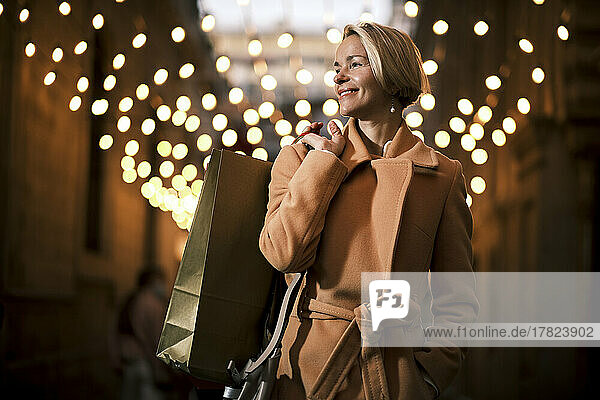 Happy woman holding shopping bag at night