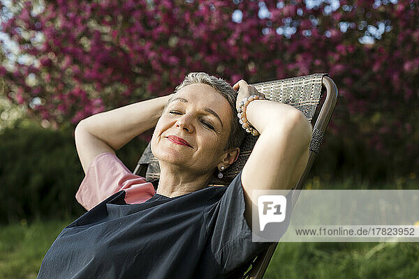 Lächelnde Frau mit geschlossenen Augen ruht im Garten