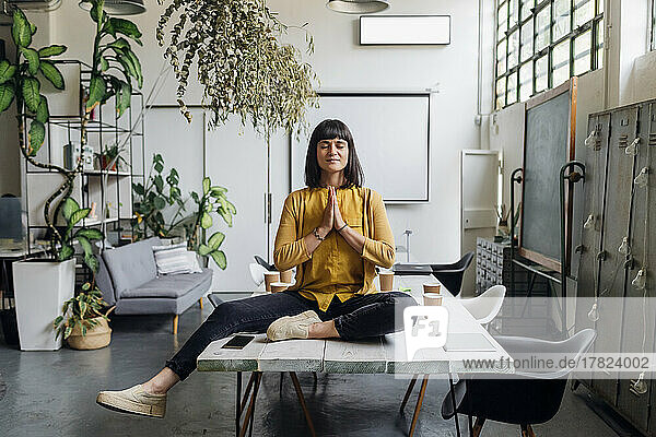 Geschäftsfrau meditiert mit gefalteten Händen auf dem Schreibtisch am Arbeitsplatz