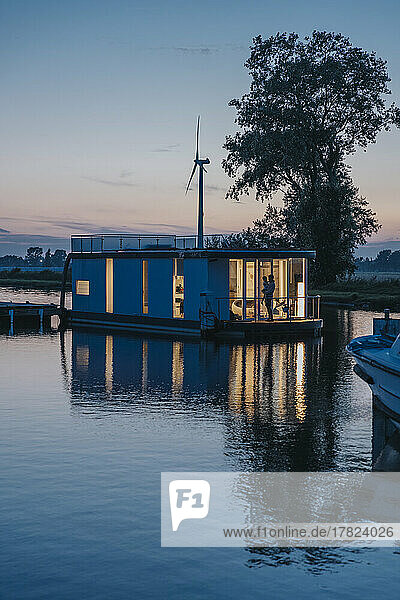 Illuminated houseboat with reflection on Yser River at sunset