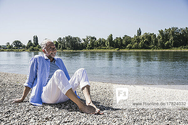 Lächelnder älterer Mann sitzt am Flussufer