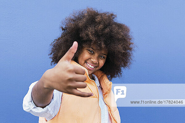 Smiling girl gesturing shaka sign against blue background
