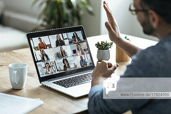 Businessman greeting colleagues on video conference through laptop at home