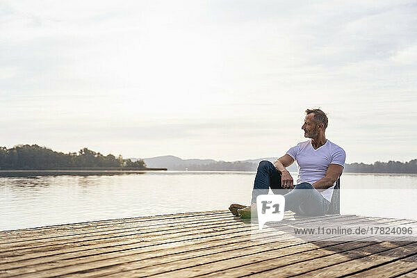 Mature man sitting on jetty at lake