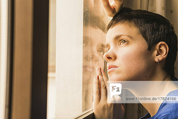 Frau mit kurzen Haaren lehnt zu Hause am Fenster