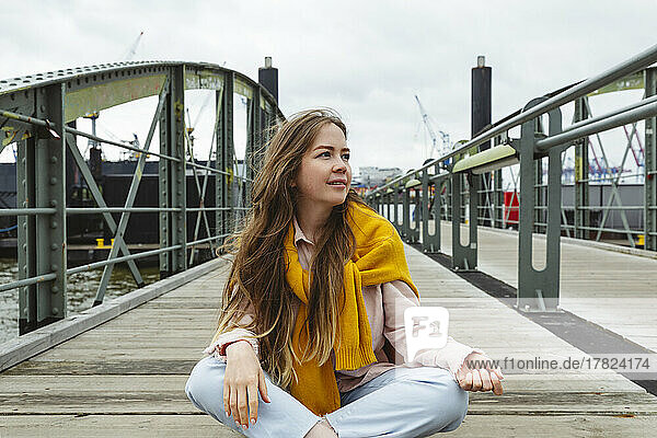 Smiling young woman with long brown hair sitting on footbridge