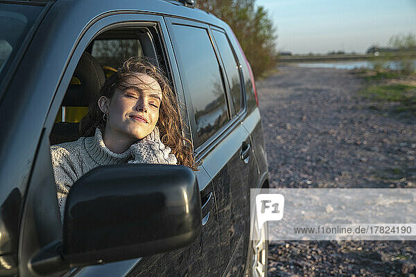 Lächelnde Frau mit geschlossenen Augen sitzt im Auto